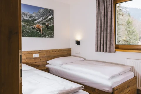Schlafzimmer im Appartement mit zwei Einzelbetten, Holz-Kopfteil, Nachttischlampe, Landschaftsbild an der Wand und Vorhang am